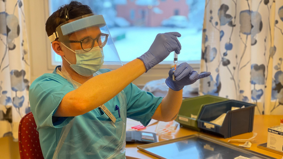 Sjuksköterska med skyddsutrustning drar upp vaccin i en spruta.