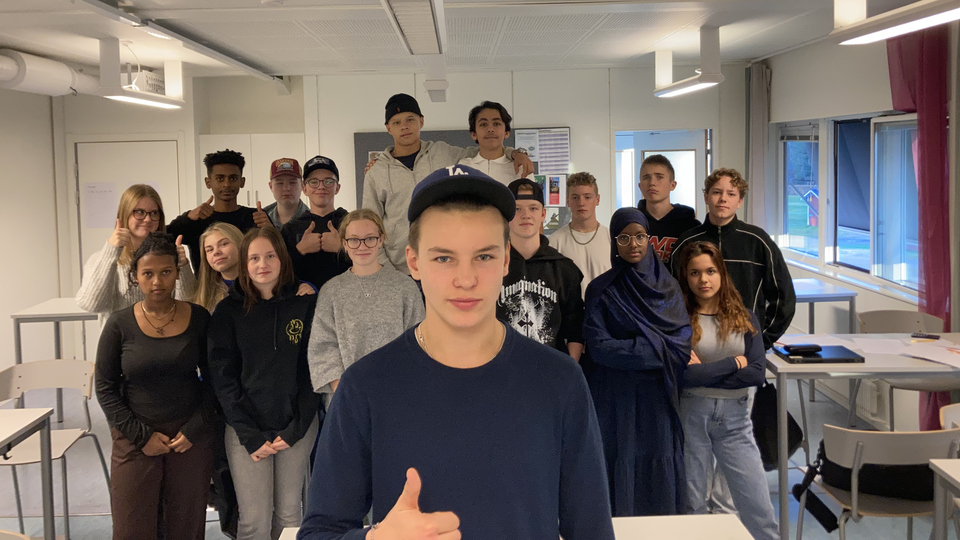 En klass i ett klassrum med en man som ger tummen upp.