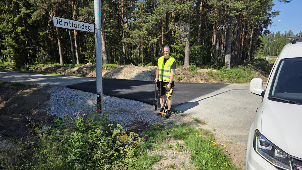En man i gul väst står  på en väg bredvid en gatuskylt.