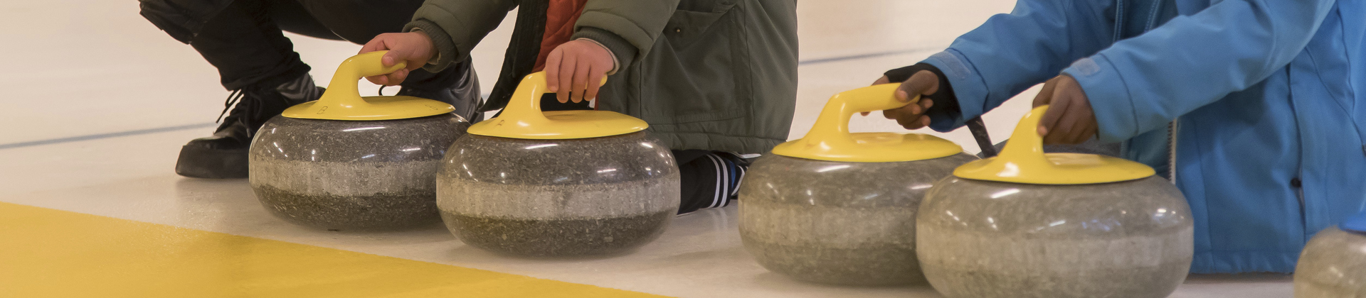 Barnhänder som håller curlingklot på en curlingbana