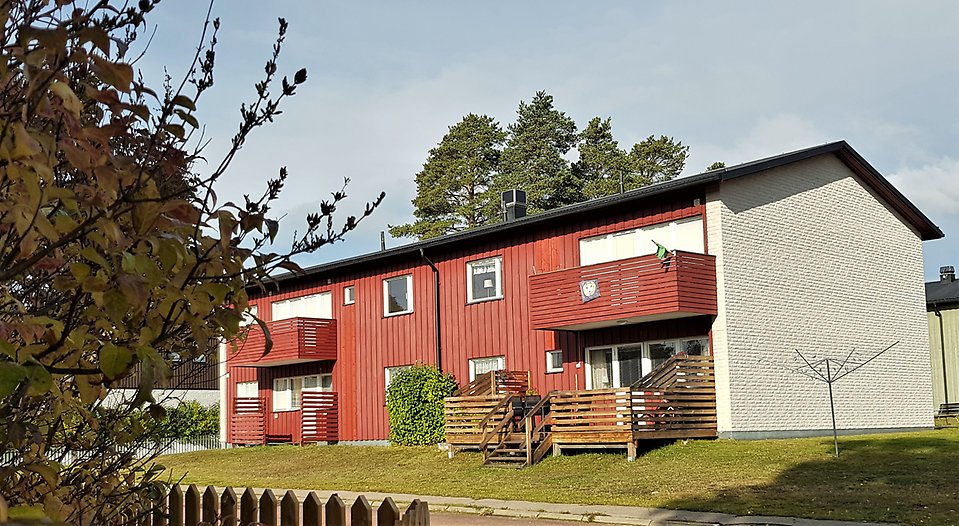 Ett rött flerfamiljshus med två våningar och balkonger och en uteplats. Ett staket i förgrunden. 